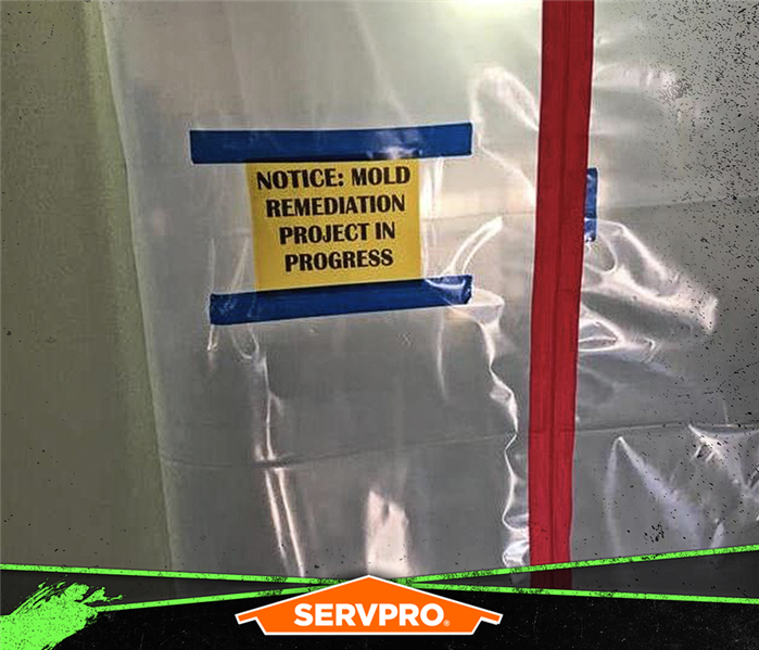 Plastic barrier taped to a wall with a sign saying: NOTICE: MOLD REMEDIATION PROJECT IN PROGRESS