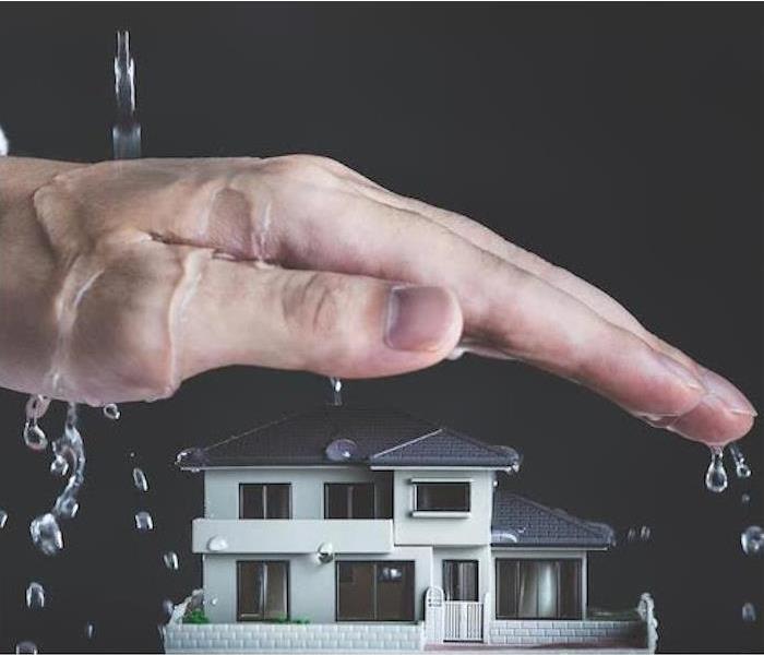 A hand covering a home from water